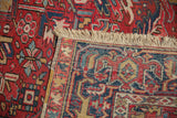 Folded edge of vintage Gorevan carpet, with worn cherry red, navy, gold geometric patterns and fringe.