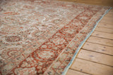 Angled view of a vintage Meshed carpet's low pile and copper-toned floral border.