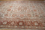Angled view of a distressed Persian rug showing its textured floral field and rich terra cotta border.
