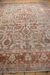 Low angle view of a distressed vintage carpet, emphasizing the texture of its ivory and terra cotta floral pattern.