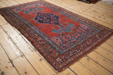 A traditional Persian Bijar rug from an angle, showing the bold ram's horn finials and Herati design.