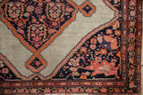 A bird and expressive leaves within the navy blue spandrel of an antique Malayer rug.