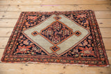 Tattered side of an antique Malayer rug, detailing its floral border in navy and terra cotta.