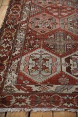 Angled view of a distressed Baktiari rug's serrated border and geometric field in time-softened chestnut and rose tones.