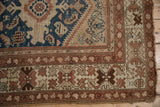 Vintage Caucasian rug corner with geometric patterns, low pile wear, and tattered ends.