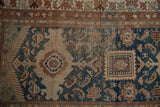 Distressed texture of a vintage Caucasian rug, featuring navy, beige, and rust geometric patterns.
