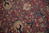 A detailed view of the antique Tabriz carpet's cochineal red field with intricate palmettes and scrolling vinery.