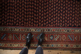 Overhead view showing the dense boteh pattern and wide floral border of a vintage Kurd rug.