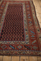 Angled view of the navy boteh field and intricate, multi-banded rust border on a vintage Kurd rug.