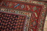 Corner detail of a vintage Kurd rug's geometric rust border and dark navy field with repeating botehs.