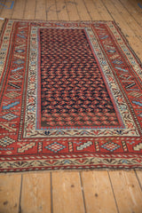 A vintage Kurd rug's geometric boteh field and rust-red border system viewed from an angle.