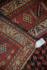 Close-up of a vintage Kurd rug's geometric border in rust, brown, and ivory with a paper tag.