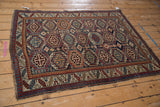 Angled perspective of a vintage Caucasian rug with repeating octagonal guls in navy blue, red, and gold.