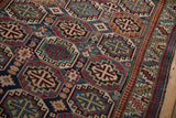 Angled view of repeating octagonal guls and the geometric border of a vintage Caucasian rug.