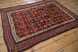 Angled view of an antique Caucasian rug showing its dense geometric patterns in red, blue, and pink.