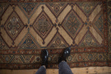 Overhead view of an antique Kurd rug's geometric diamond medallions on an abrashed camel field.