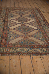 Angled view of an antique Kurd rug, highlighting the repeating diamond medallions on its abrashed camel field.