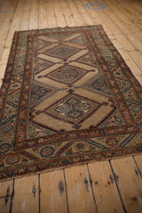 Angled perspective of an antique Kurd rug with diamond medallions on an abrashed camel ground.
