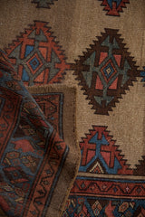 Folded vintage Kurd runner revealing its hand-knotted texture, geometric guls, and camel ground.