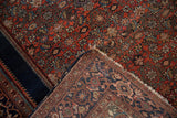 Folded Farahan Sarouk rug revealing its hand-knotted back, worn red-navy pattern, and tattered fringe.