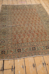Antique Tabriz rug corner with fringe, worn terracotta boteh field, and floral border.