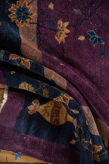 Plush folded pile of Nichols rug, plum, navy, gold vinery, and visible white knots.
