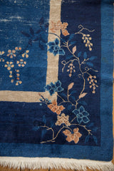 Vintage Peking carpet corner showing indigo field, beige stripe, vinery, wear, and fringe.