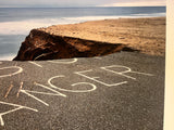 The word DANGER painted on a road that is crumbling into the ocean from coastal erosion.