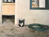 Color photograph of a garage with a peach car, a coiled green hose, and a white wall.