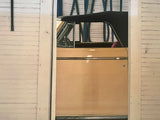Side profile of a tan vintage convertible framed by the white slatted walls of a garage.