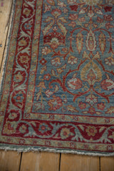 Corner of distressed Yezd runner showing worn floral field, red arabesque border, tattered edge.