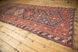 Angled view of a long antique Afshar runner with a central column of red and blue diamond medallions.