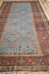 Angled view down the length of an antique Fereghan carpet, showing its powder blue field and wide red border.