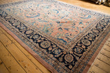 Close-up of vintage Laristan carpet corner: navy border, dusty rose field, blue floral vines.