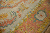 Blush, saffron, and dusty teal palmette motifs along the serrated Oushak border, with varying pile and selvage.