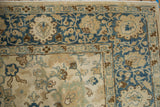 The distressed corner of a Tabriz rug with dusty blue arabesques and ivory palmettes.