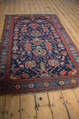 Angled view of a vintage Malayer rug showing its full length and intricate pattern on a navy blue field.
