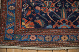 Corner of a vintage Malayer rug showing stylized birds in a navy field beside colorful floral borders.