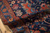 Angled view of a folded Malayer rug corner, highlighting its gem-toned floral motifs on a navy ground.
