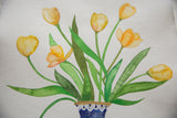 Close view of watercolor yellow tulips and green leaves in a blue patterned vase.