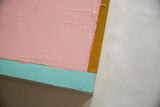 Abstract painting detail: thick pastel pink, turquoise, mustard yellow impasto on deep wood.