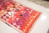 Angled close-up of the geometric rug print showing the glossy finish over red and pink tones.