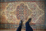 A person's view looking down at the distressed Herati medallion of a vintage Persian Malayer rug.