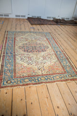 Angled gallery view of a distressed vintage Malayer rug with a scalloped medallion and ivory field.