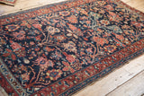 Vintage Hamadan rug's worn madder red border, navy blossom field, and tattered side edge.