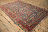 Worn corner of antique Persian Malayer rug, with cherry red border, slate blue Herati motif, and tattered fringe.