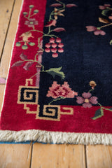 Art Deco rug corner: red border, geometric pattern, navy field, blush floral vinery.