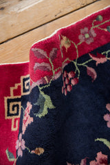 Art Deco rug's plush navy pile, delicate vinery, blush florals, and red geometric border.