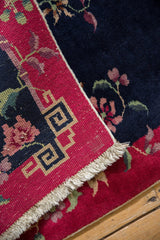 Fringed corner of a Vintage Nichols Art Deco rug, showcasing red geometric border and navy floral pattern.