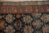 Close-up of vintage Caucasian rug borders, navy field floral palmettes, and visible knot heads.